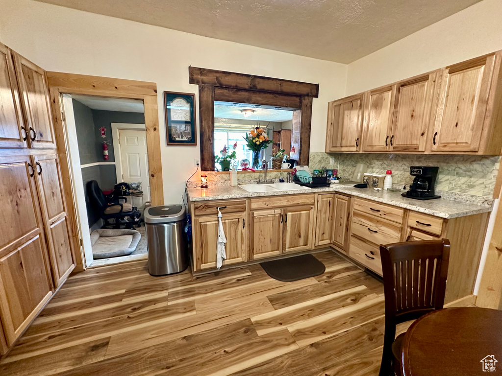 Kitchen with backsplash, light stone counters, sink, and hardwood / wood-style floors