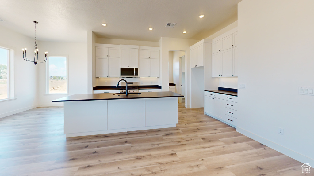 Kitchen featuring light wood-type flooring, a center island with sink, white cabinetry, a chandelier, and sink