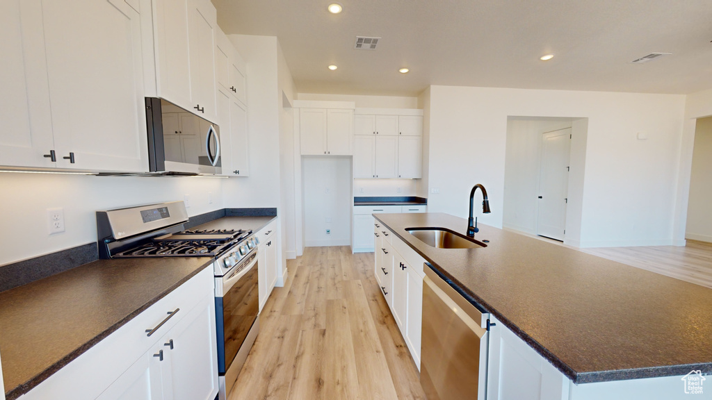 Kitchen with stainless steel appliances, an island with sink, light wood-type flooring, sink, and white cabinetry