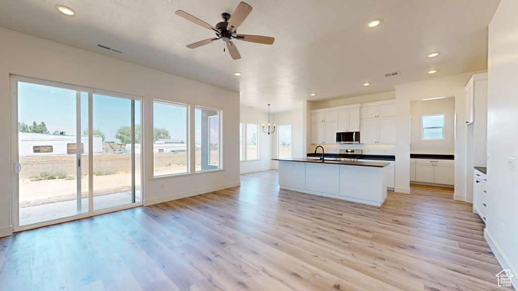 Kitchen featuring ceiling fan, light wood-type flooring, white cabinetry, and an island with sink