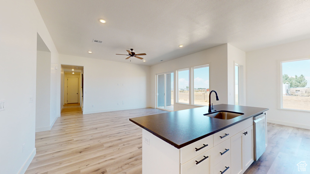 Kitchen featuring a healthy amount of sunlight, a center island with sink, sink, and white cabinetry