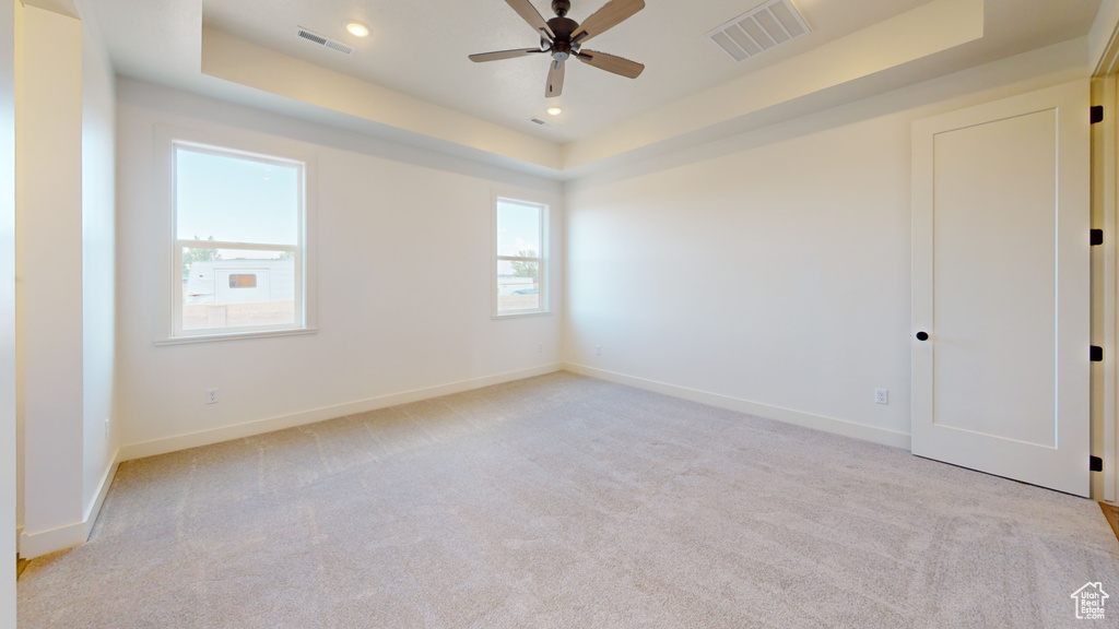 Carpeted empty room featuring ceiling fan and a raised ceiling