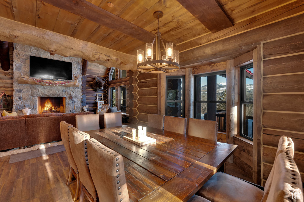 Dining space featuring a notable chandelier, wooden ceiling, dark wood-type flooring, a stone fireplace, and log walls