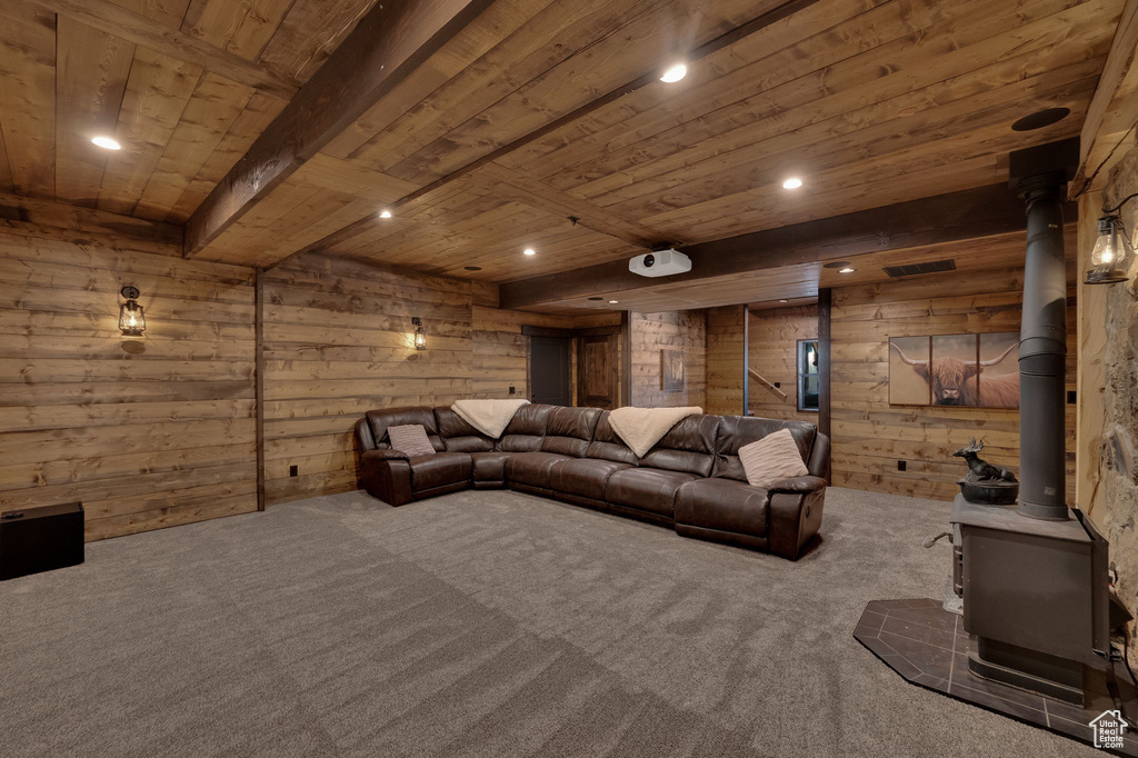 Cinema room with beamed ceiling, wooden walls, a wood stove, wood ceiling, and dark carpet