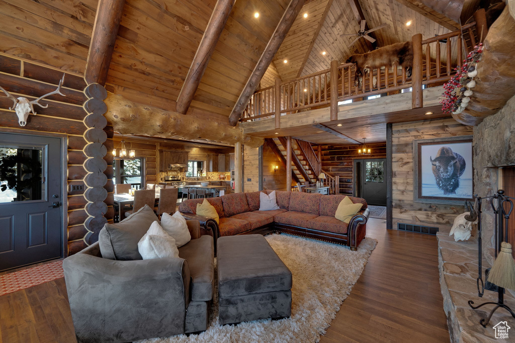 Living room with rustic walls, wooden ceiling, high vaulted ceiling, ceiling fan with notable chandelier, and dark hardwood / wood-style flooring