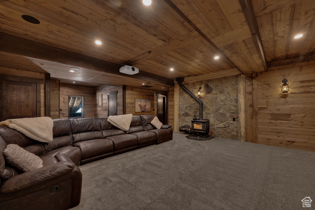 Cinema room featuring wooden walls, beam ceiling, a wood stove, wood ceiling, and carpet floors