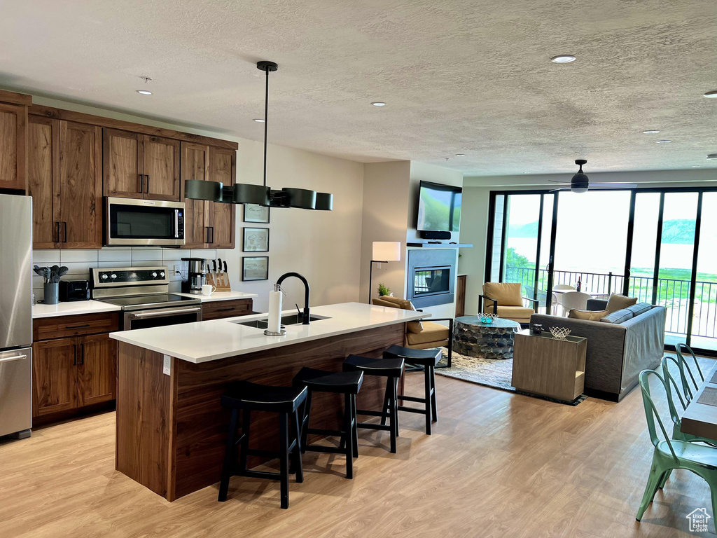 Kitchen with appliances with stainless steel finishes, a center island with sink, sink, light hardwood / wood-style flooring, and decorative light fixtures