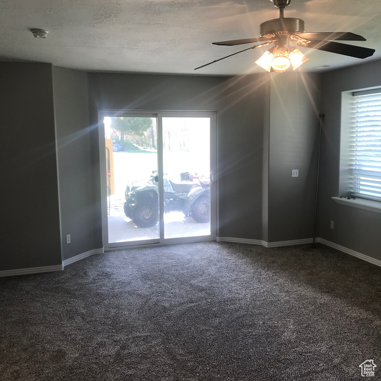 Spare room with plenty of natural light, ceiling fan, a textured ceiling, and dark carpet