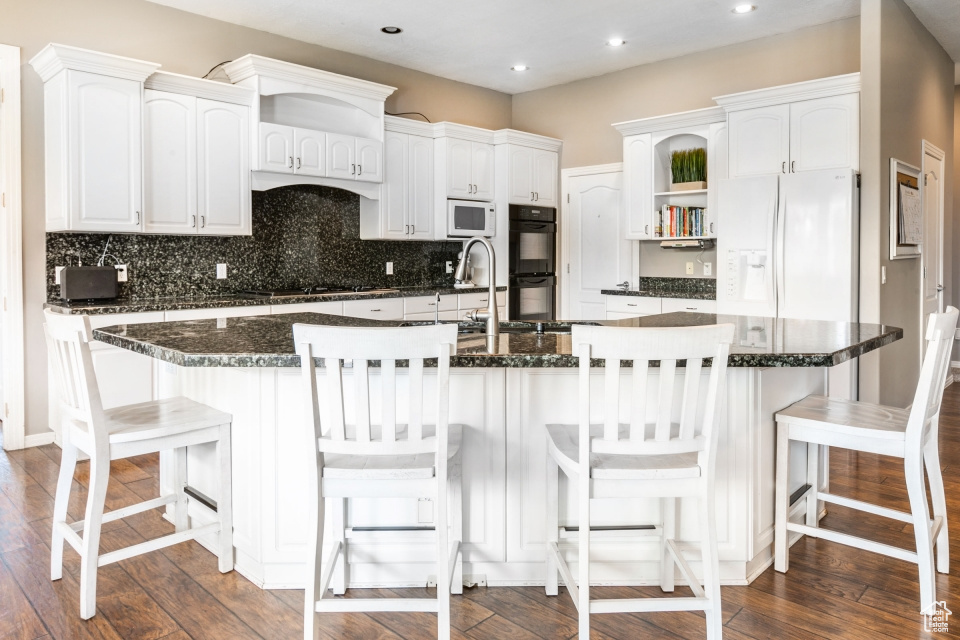 Kitchen featuring black appliances, white cabinetry, a breakfast bar area, and a center island with sink