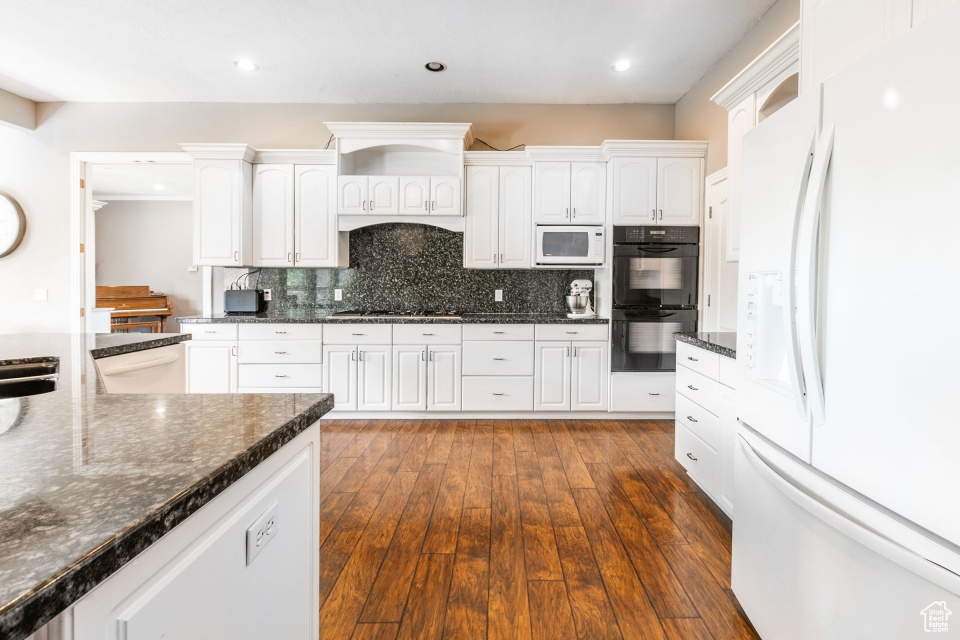 Kitchen featuring white appliances, dark stone countertops, dark hardwood / wood-style floors, backsplash, and white cabinets