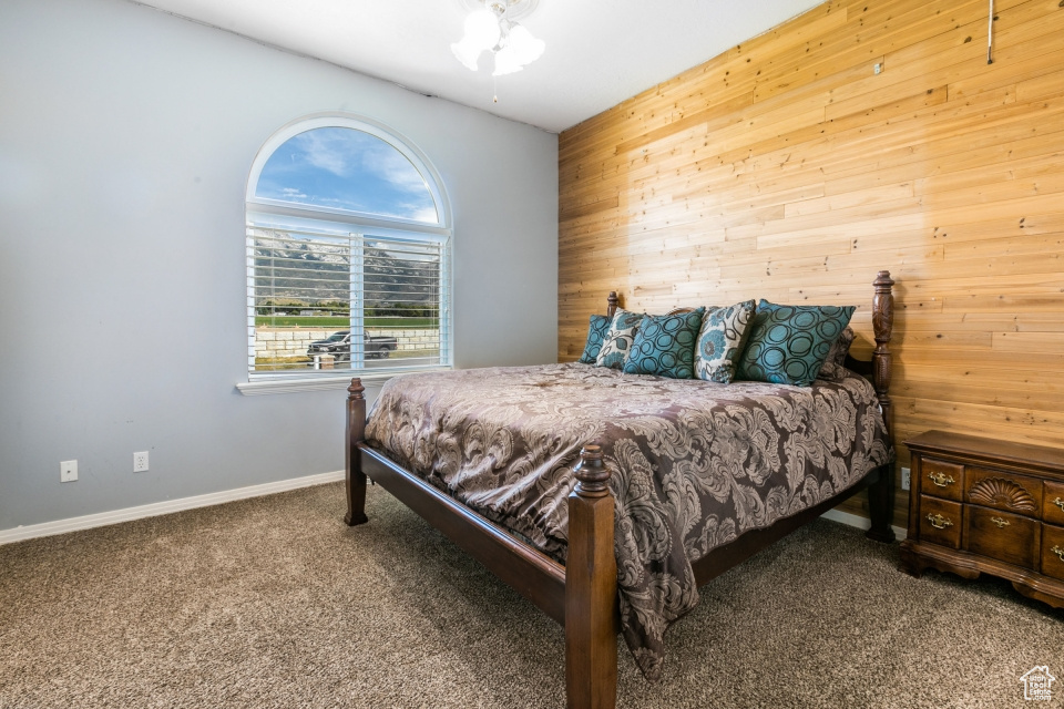Carpeted bedroom with wooden walls and ceiling fan