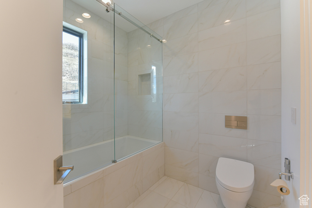 Bathroom with toilet, a shower with door, tile walls, and tile floors