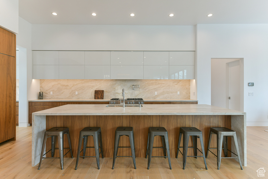 Kitchen featuring sink, white cabinets, tasteful backsplash, a center island with sink, and light wood-type flooring