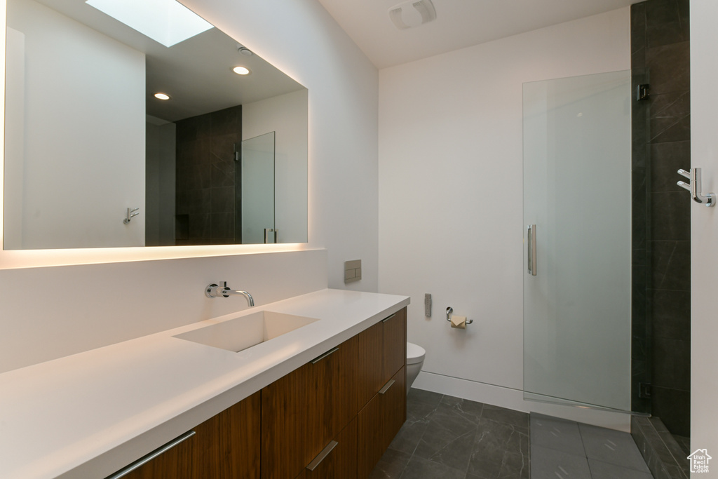 Bathroom with vanity, a skylight, a shower with door, toilet, and tile floors
