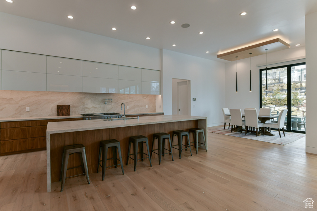 Kitchen with white cabinetry, an island with sink, light wood-type flooring, and a breakfast bar area