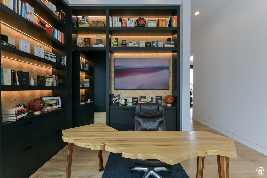 Home office with light hardwood / wood-style flooring and built in shelves