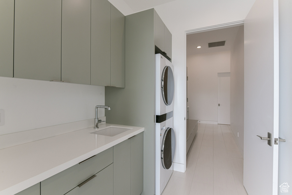 Laundry area featuring light tile floors, sink, stacked washing maching and dryer, and cabinets