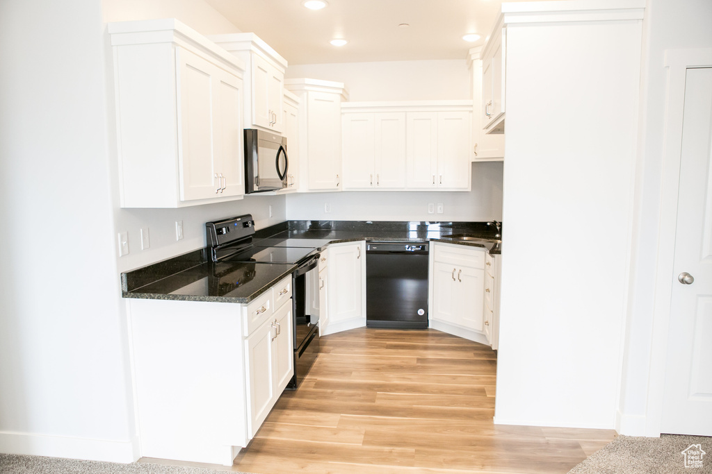 Kitchen with white cabinetry, sink, dark stone countertops, black appliances, and light wood-type flooring