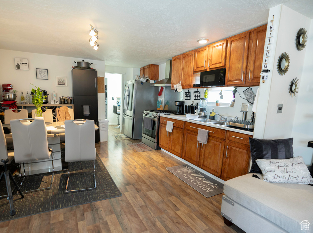 Kitchen featuring gas range, track lighting, sink, hardwood / wood-style flooring, and wall chimney exhaust hood