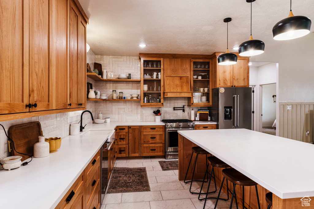 Kitchen with tasteful backsplash, appliances with stainless steel finishes, light tile floors, sink, and pendant lighting