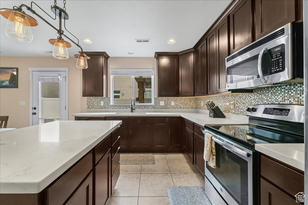 Kitchen featuring appliances with stainless steel finishes, tasteful backsplash, decorative light fixtures, and dark brown cabinetry