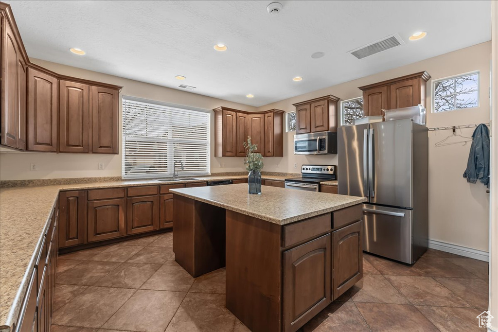 Kitchen featuring a kitchen island, dark tile flooring, stainless steel appliances, and plenty of natural light