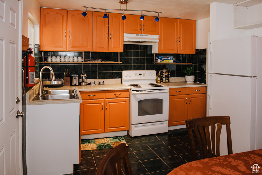 Kitchen featuring white appliances, tasteful backsplash, dark tile floors, and sink