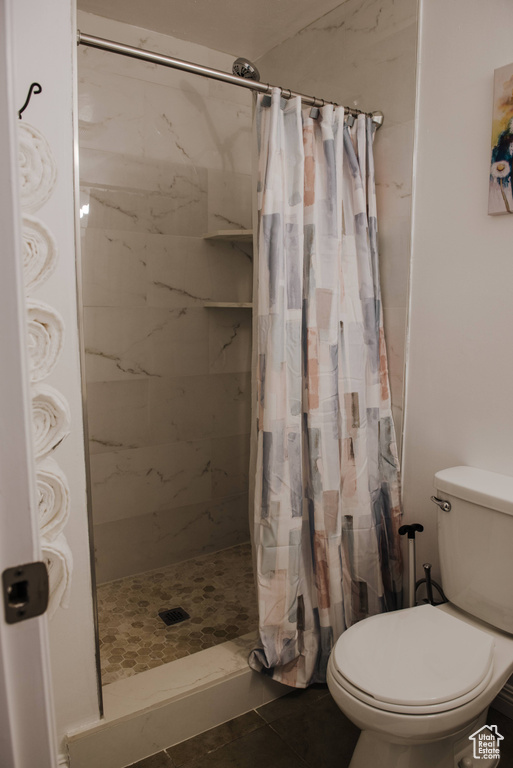 Bathroom featuring toilet, a shower with shower curtain, and tile flooring