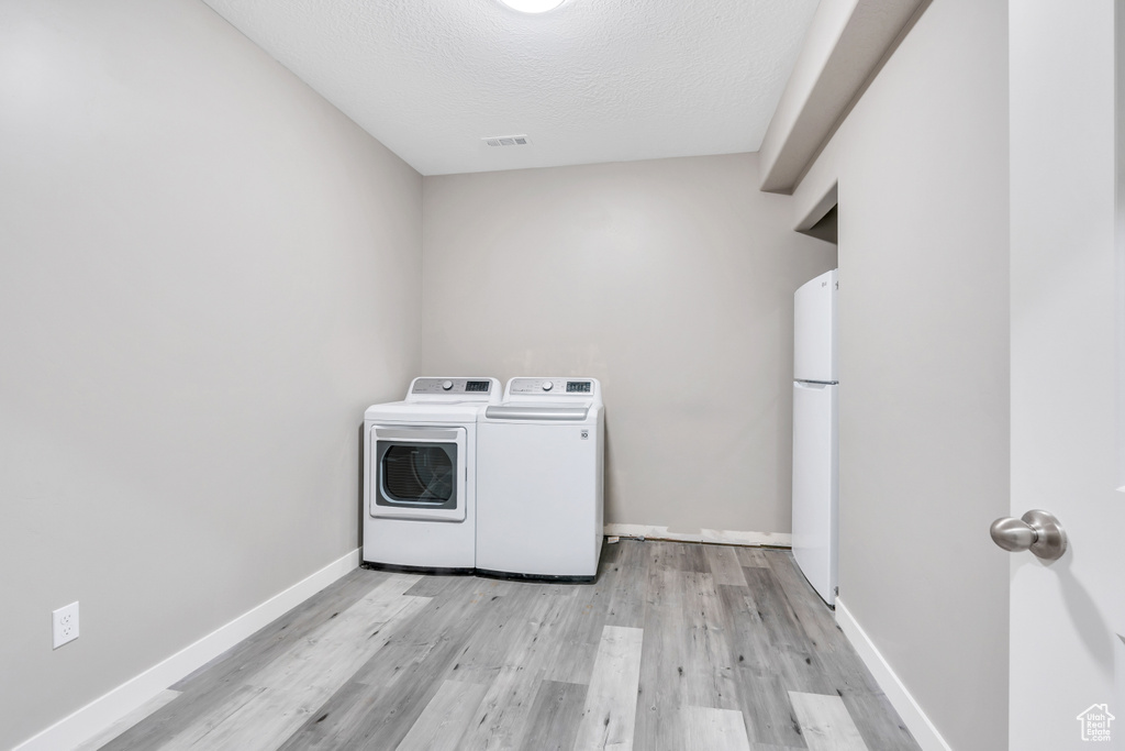 Washroom with a textured ceiling, washing machine and clothes dryer, and light hardwood / wood-style flooring
