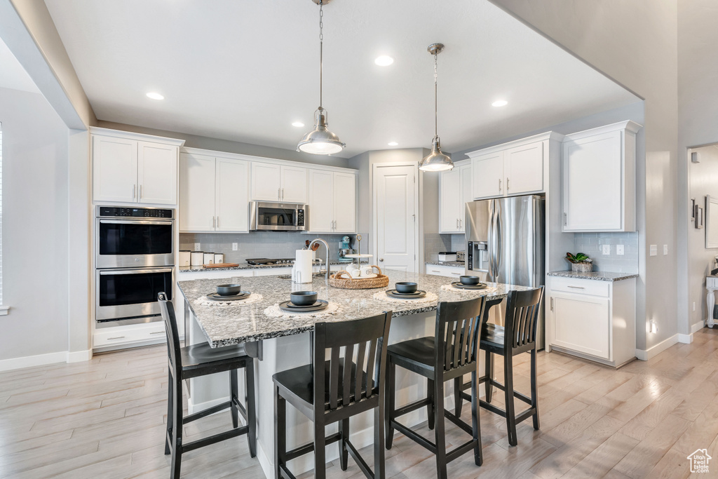Kitchen with white cabinetry, a breakfast bar, tasteful backsplash, light hardwood / wood-style flooring, and stainless steel appliances