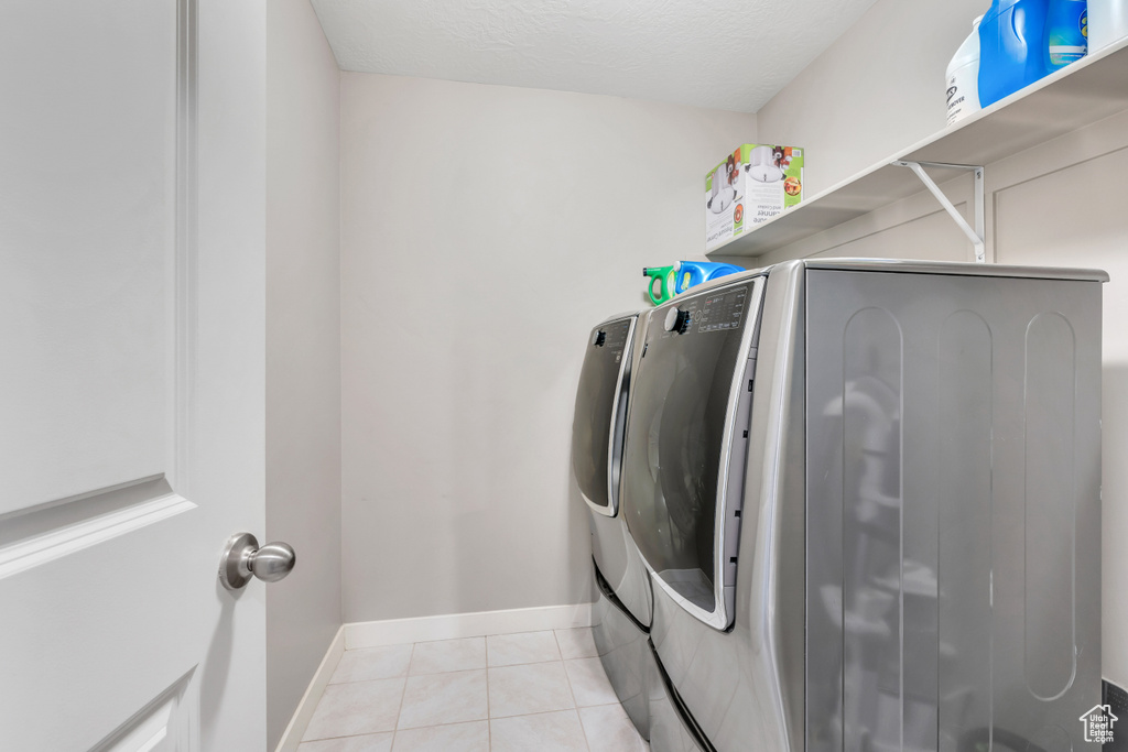 Washroom with light tile floors and washing machine and clothes dryer