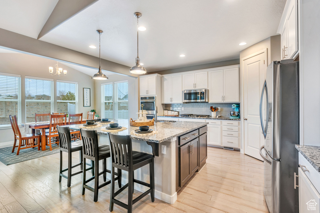 Kitchen with appliances with stainless steel finishes, vaulted ceiling, an inviting chandelier, a center island with sink, and white cabinetry