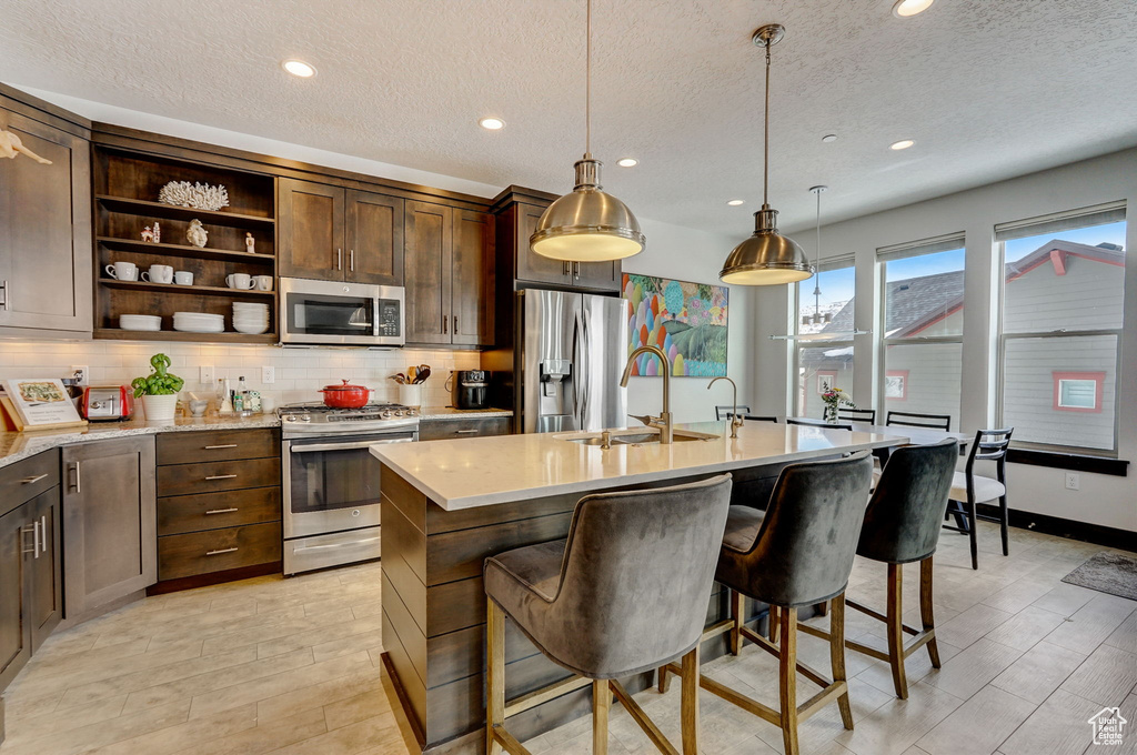 Kitchen with appliances with stainless steel finishes, a breakfast bar area, hanging light fixtures, and a center island with sink