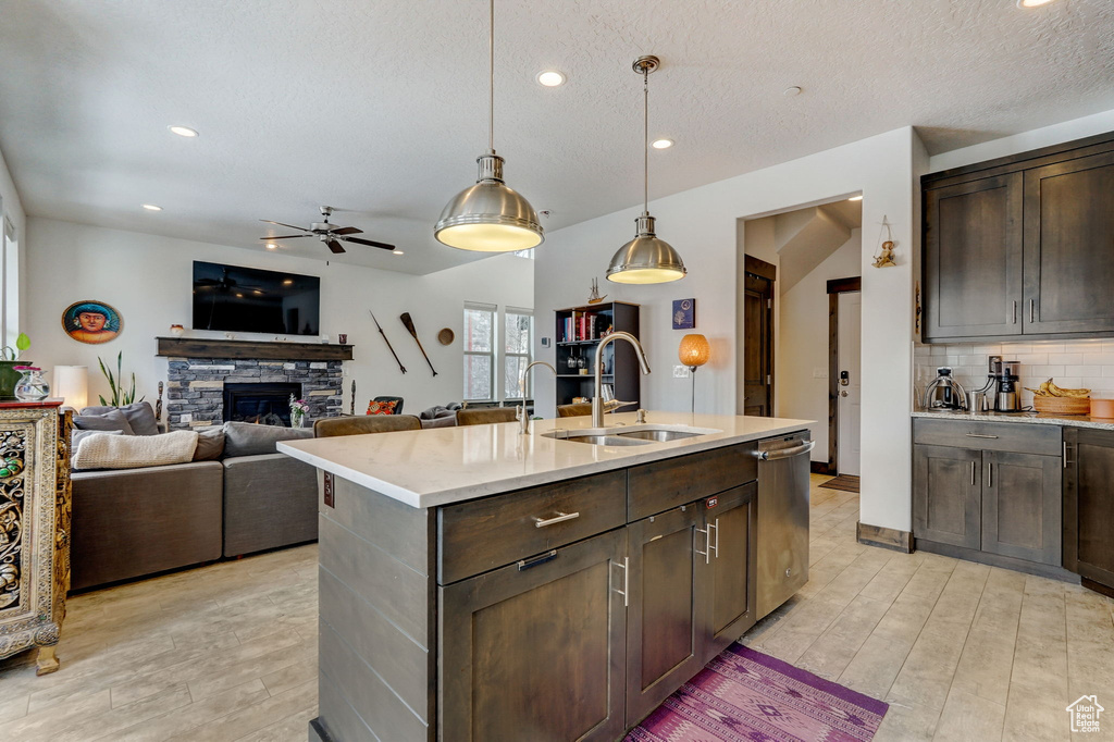 Kitchen featuring a fireplace, pendant lighting, stainless steel dishwasher, a center island with sink, and ceiling fan