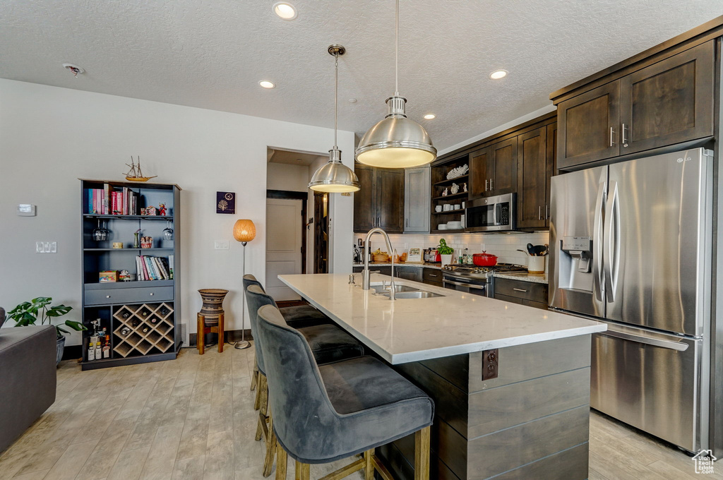Kitchen with sink, appliances with stainless steel finishes, light hardwood / wood-style flooring, a breakfast bar area, and pendant lighting