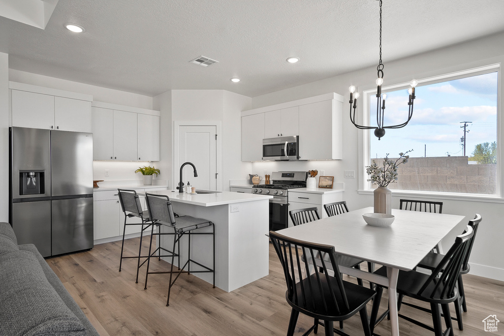 Kitchen featuring white cabinets, a chandelier, light hardwood / wood-style floors, a center island with sink, and stainless steel appliances