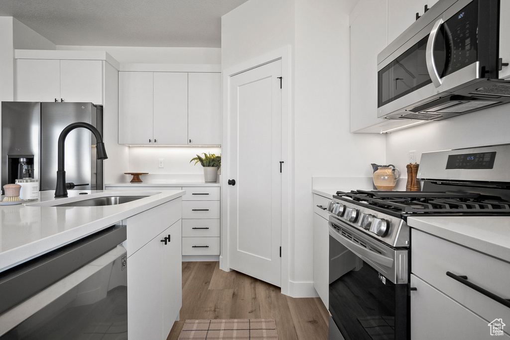 Kitchen with white cabinetry, light wood-type flooring, stainless steel appliances, and sink