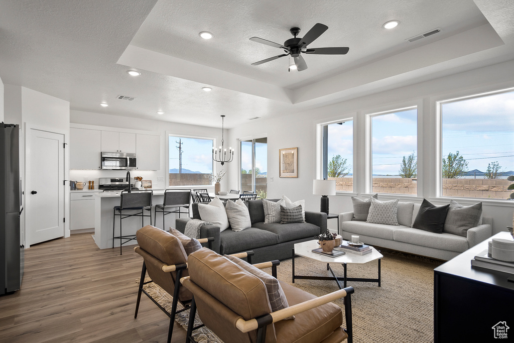 Living room with ceiling fan with notable chandelier, a raised ceiling, and light hardwood / wood-style floors