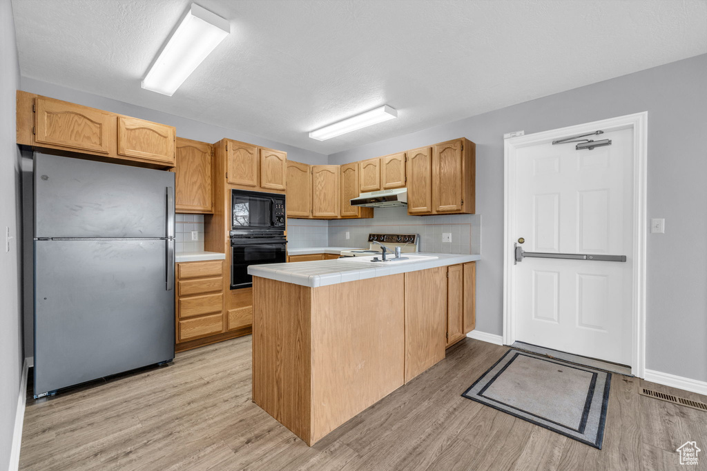 Kitchen with black appliances, light hardwood / wood-style flooring, tasteful backsplash, and kitchen peninsula