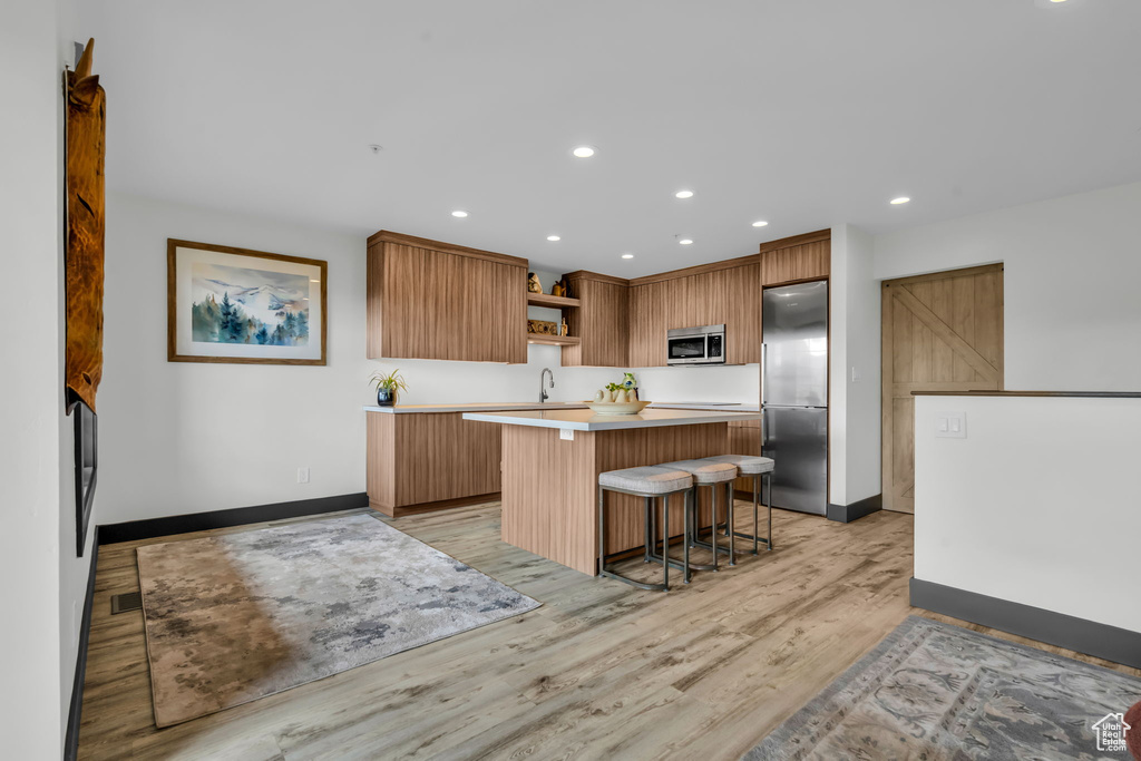 Kitchen with appliances with stainless steel finishes, light hardwood / wood-style floors, sink, a breakfast bar, and a kitchen island