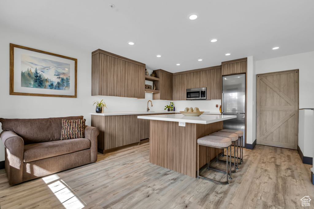 Kitchen featuring a kitchen island, stainless steel appliances, light hardwood / wood-style floors, and a kitchen bar