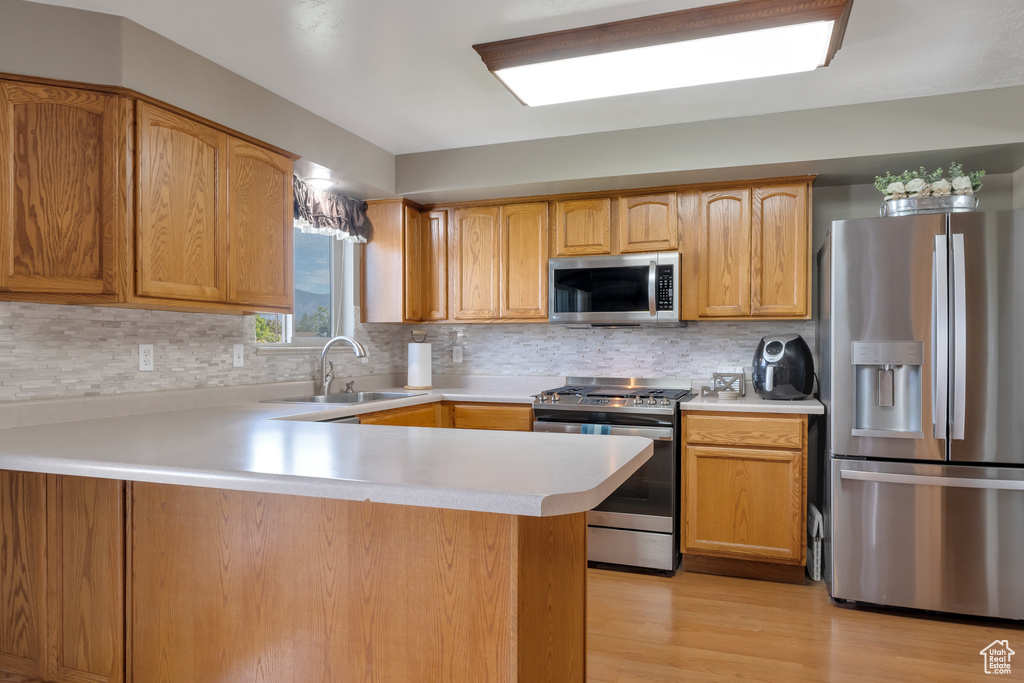 Kitchen with appliances with stainless steel finishes, light wood-type flooring, tasteful backsplash, and sink