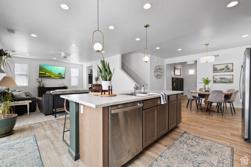 Kitchen featuring stainless steel appliances, a kitchen island with sink, sink, pendant lighting, and light wood-type flooring
