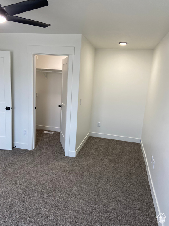 Empty room featuring ceiling fan and dark colored carpet