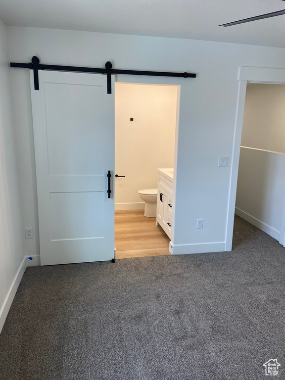 Unfurnished bedroom with ensuite bath, light carpet, and a barn door