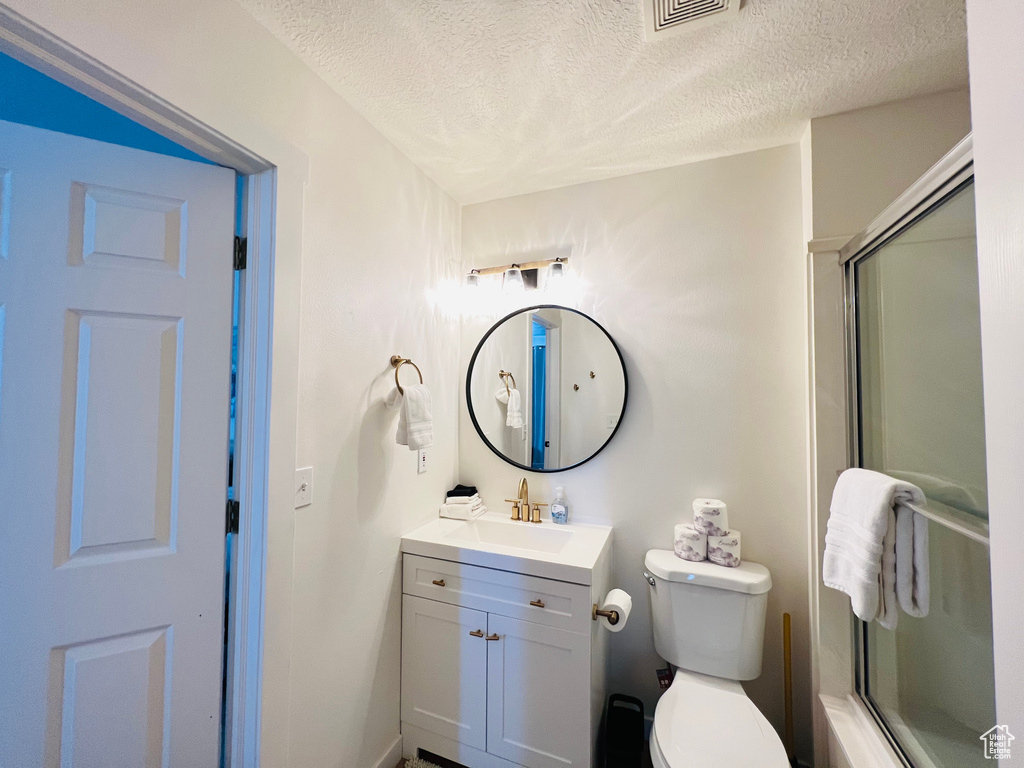 Full bathroom with vanity, toilet, a textured ceiling, and bath / shower combo with glass door