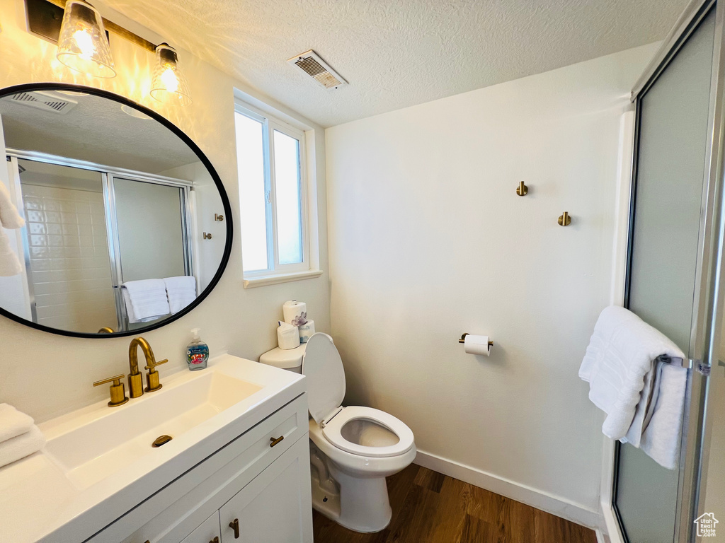 Bathroom with a shower with door, hardwood / wood-style floors, a textured ceiling, toilet, and vanity