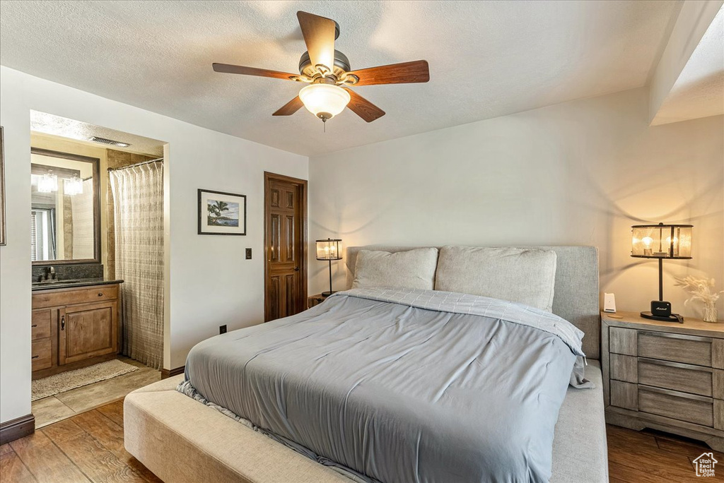 Bedroom with ensuite bathroom, light wood-type flooring, a textured ceiling, and ceiling fan