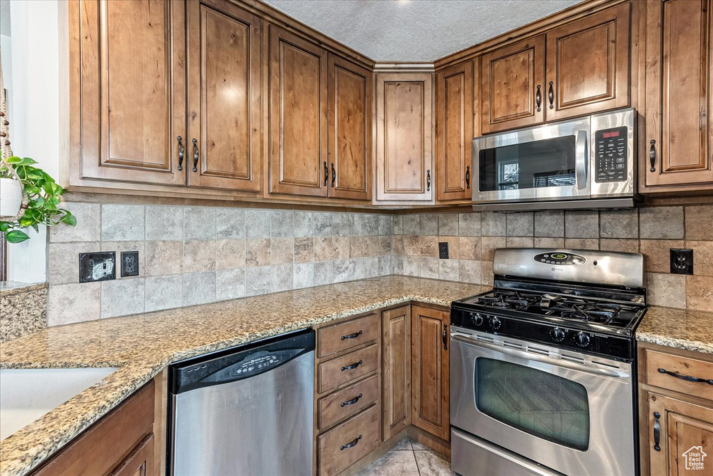 Kitchen with appliances with stainless steel finishes, backsplash, and light stone counters