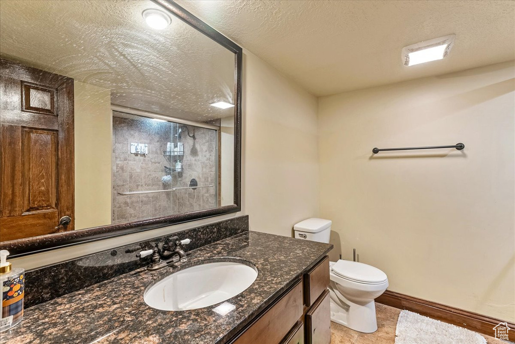 Bathroom with vanity with extensive cabinet space, tile floors, a textured ceiling, and toilet